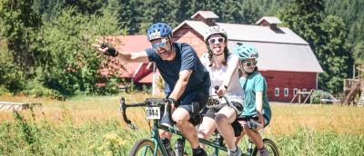 A family of 3 rides a tandem on STP 2025 past the iconic red barn. Photo by MarathonFoto.