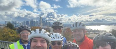 Several cyclists in front of a view of the Space Needle, Elliot Bay, and Seattle Skyline
