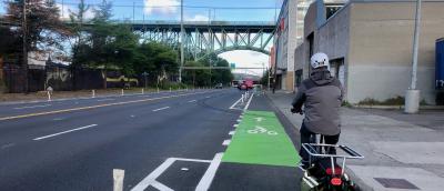 A cyclist riding an e-cargo bike in a green painted flexpost protected bike lane on Dearborn Street approaching the José Rizal Bridge