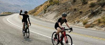 Riders smile and wave while riding up a hill on the Lake Chelan Tour.