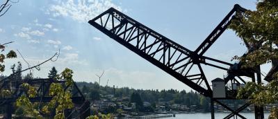 A steel railroad bridge over Salmon Bay is raised diagonally to allow boats to pass underneath on a sunny day