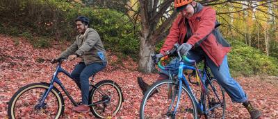 Two people bike through fallen autumn leaves. 