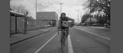 A man bikes down a street holding a box.