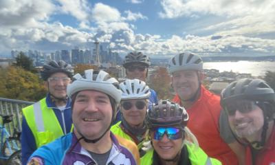 Several cyclists in front of a view of the Space Needle, Elliot Bay, and Seattle Skyline