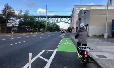 A cyclist riding an e-cargo bike in a green painted flexpost protected bike lane on Dearborn Street approaching the José Rizal Bridge