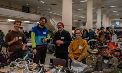 A group of vendors sits or stands behind a table of good and smiles at the camera.