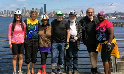 Seven riders in casual clothing including three men and four women of varying ages and ethnicities.