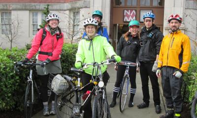 Three women and two men with bike helmets and casual clothing prepare to ride