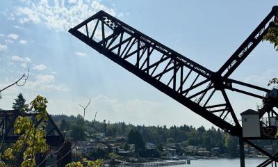 A steel railroad bridge over Salmon Bay is raised diagonally to allow boats to pass underneath on a sunny day