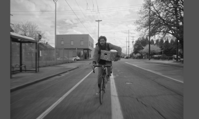 A man bikes down a street holding a box.